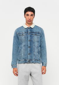 Jeansjacka i ljusblått med en imitation av fårskinnskrage. Har knappstängning, sidofickor och stickade detaljer genomgående.