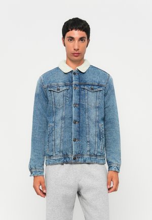 Chaqueta de mezclilla en azul claro con cuello de pelaje sintético. Presenta cierre de botones, bolsillos laterales y detalles de costura en toda la prenda.