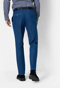 Pantalon en denim bleu avec un design à jambes droites, style cinq poches, et une ceinture noire, associé à des chaussures en suede noir.