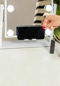 Vit sminkspegel med LED-lampor, som håller en smartphone i ett svart fodral. Inkluderar en kompakt låda på sidan med etiketten "Morphe x Nyane".