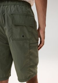 Shorts cargo verdi realizzati in tessuto leggero. Presentano una vita elastica, tasche laterali e un motivo a strisce con texture.