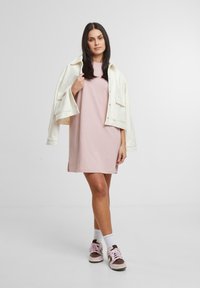 Ružičasta pamučna haljina opuštenog kroja s bočnim prorezima, složena s kremasto bijelim oversized sakoom. Uparena s smeškim i ružičastim tenisicama.