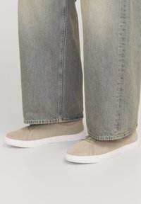 Zapatillas de ante beige con suelas de goma blanca, que presentan cordones y detalles de costura, combinadas con unos vaqueros de denim ligero de corte holgado en color azul claro.