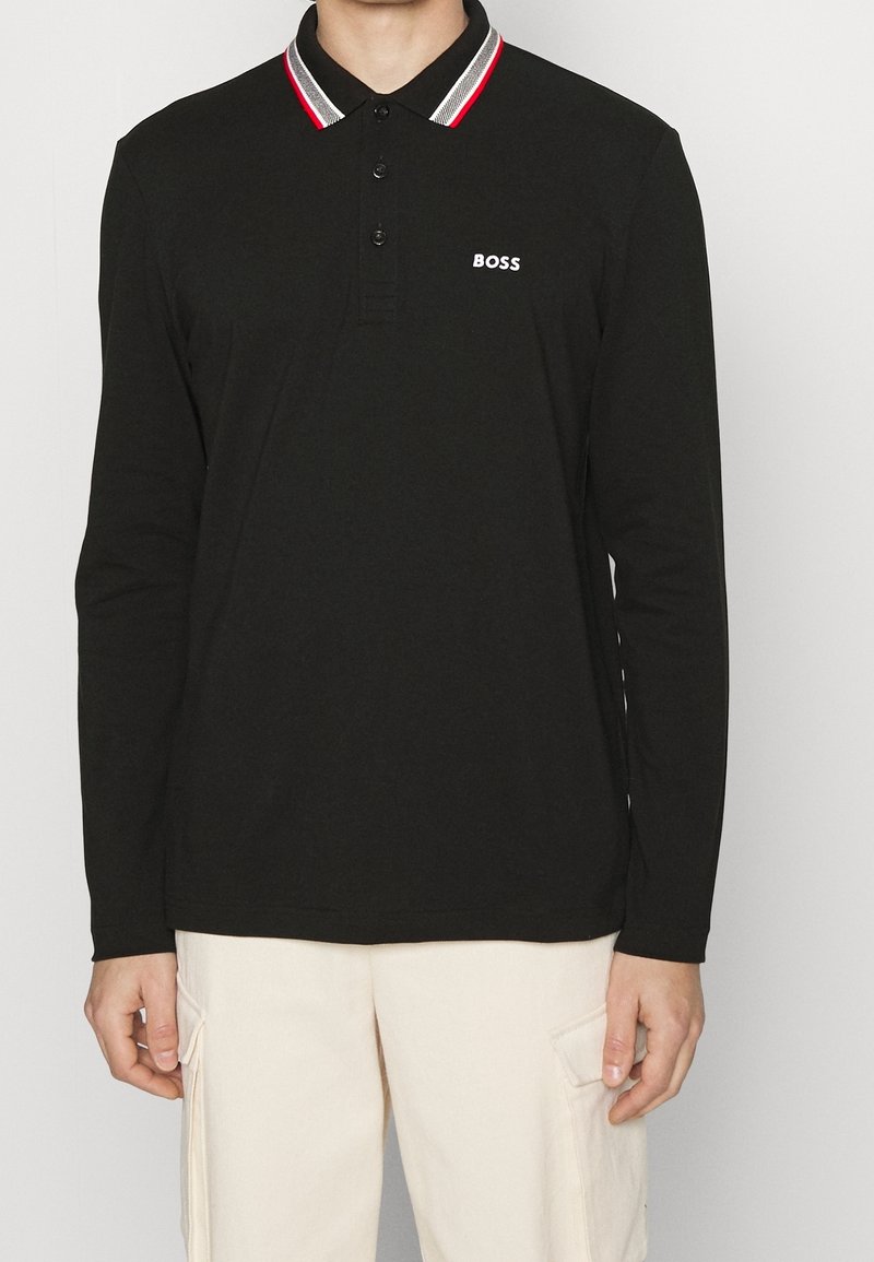 Svart långärmad pikétröja med en randig krage i röd, vit och svart, med en knäppning framtill och en logotyp på bröstet.