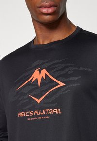 Schwarzes Sportshirt mit einem orangefarbenen Berg-Logo und dem Text "ASICS FUJITRAIL" mit darunterstehenden Koordinaten, aus einem glatten, leichten Material gefertigt.