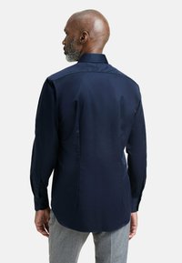 Camicia a maniche lunghe blu navy con colletto aperto, texture liscia e polsini con bottoni, caratterizzata da una yoke posteriore e un orlo curvo.