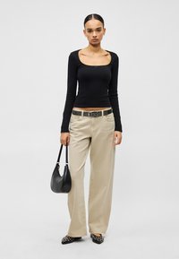 Juodas ilgomis rankovėmis viršus su kvadratine iškirpte, kreminės spalvos plačios kelnės, juodas diržas su kniedėmis ir juoda petinė rankinė. Smailiapadžiai batai su kniedėmis.