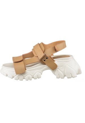 Vaaleanruskeat sandaalit paksulla valkoisella pohjalla, joissa on leveät hihnat ja säädettävät soljet. Sileä pinta ja pyöreä varvasmuoto.