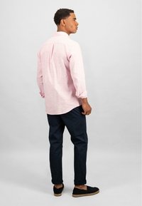 Camicia a maniche lunghe rosa chiaro con colletto a bottoni, abbinata a pantaloni blu navy e espadrillas nere. Tessuto morbido con una vestibilità comoda.