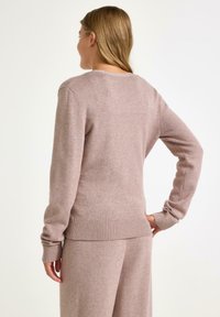 Jasnoróżowy sweter wykonany z miękkiego materiału dzianinowego, z prążkowanym dołem i mankietami, klasycznym okrągłym dekoltem oraz dopasowanym krojem.