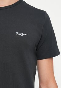 Tricou din bumbac negru cu mâneci scurte, având un logo alb "Pepe Jeans" brodat în zona stângă a pieptului. Textură netedă.