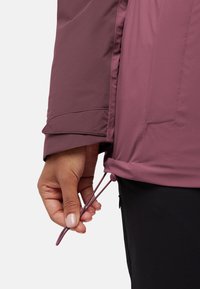 Bordeauxjack met een gladde textuur, voorzien van een trekkoord aan de onderzijde. De mouw heeft een gedeeltelijk manchetontwerp voor een verstelbare pasvorm.