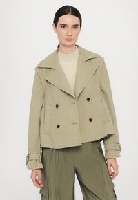 Khaki dvouřadový kabát s velkými klopami, knoflíky a manžetami se širokým lemem. Vyroben z hladkého materiálu, má zkrácený střih a boční kapsy.