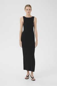 Vestido preto sem mangas com uma silhueta ajustada, apresentando tachas prateadas ao longo do decote e um corte reto até a bainha.