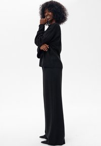 Czarny dzianinowy sweter z długimi rękawami w połączeniu z dopasowaną, długą spódnicą. Sylwetka na całej długości i gładka faktura, noszone z czarnymi, spiczastymi butami.