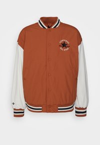 Giacca varsity arancione e bianca con bottoni a pressione, colletto e polsini a costine, caratterizzata da righe nere e bianche e dettagli con logo ricamato.