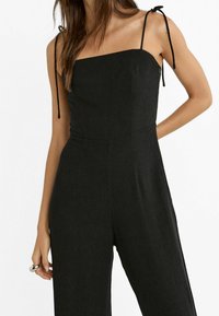 Zwarte jumpsuit met een vierkante halslijn, slanke verstelbare bandjes en een getailleerde taille, gemaakt van een gestructureerde stof, met wijde pijpen.