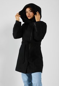 Manteau noir à capuche avec une taille ceinturée, fermeture éclair à l'avant et poches latérales ; fabriqué en tissu texturé, conçu pour la chaleur et la couverture.