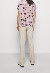 Blouse florale rose à manches courtes, avec une coupe ample et un détail de couture au dos. Associée à un pantalon beige clair et des chaussures décontractées.