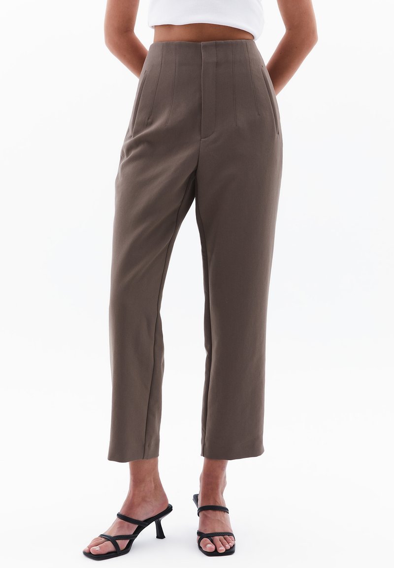 Bruine high-waisted broek met een op maat gemaakte uitstraling, verticale plooien, twee zijzakken en een ontspannen pasvorm, gecombineerd met zwarte sandaaltjes met banden.