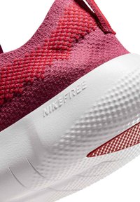 Nike Free -kenkä, jossa on teksturoitu tummanpunainen päällinen, sileä valkoinen pohja ja punaiset yksityiskohdat. Sisältää logon kaiverrettuna kylkeen ja joustavan muotoilun.