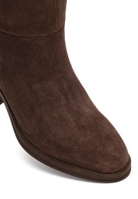 Bruine suède enkellaars met een spitse neus en subtiele textuur. Korte hak en een gladde zool, met strakke lijnen en geen zichtbare hardware.