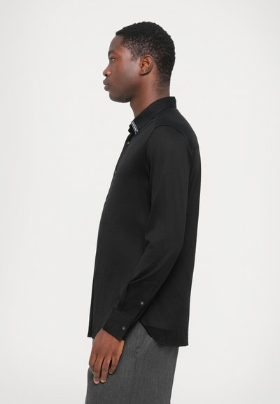 Langermet svart skjorte med standard krage, slim fit, knappestolpe og kontrastdetalj på kragen. Glatt stoff med minimal tekstur.