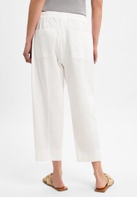 Weiße Baumwoll-Culottes mit einem elastischen Bund, ausgestattet mit zwei Gesäßtaschen und einem geraden Bein. Getragen mit beigen Riemchensandalen.