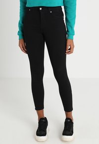 Jeans ajustados de tiro alto en color negro, con una textura suave, un corte ceñido y un diseño minimalista que incluye bolsillos frontales y un cierre de botón.