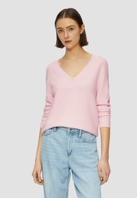 Lichtroze ribgebreide trui met een v-hals en lange mouwen, gecombineerd met lichtblauwe denim jeans. Vlezige textuur, een relaxte pasvorm en geen zichtbare patronen.