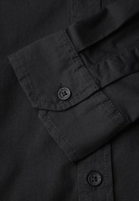 Zwarte overhemd met knopen en een opgevouwen manchet, met contrasterende stiksels en een ronde, zwarte plastic knoopdetails. Glad stoftextuur.