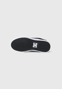 Crna potplata cipele s heksagonalnim uzorkom i bijelim DC Shoes logom u središtu, prikazana odozdo na bijeloj pozadini.