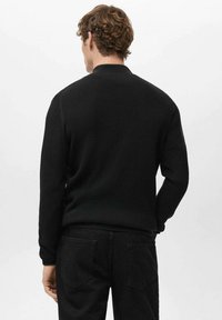 Czarny sweter w prążki z okrągłym dekoltem i długimi rękawami, w połączeniu z czarnymi spodniami z tylnymi kieszeniami. Tekstura wydaje się miękka i dopasowana.