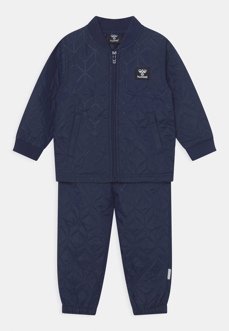 Granatowy, pikowany dres z rozpinaną kurtką i elastycznymi spodniami. Posiada wzór w romby, ściągacze oraz boczne kieszenie.