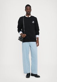 Black sweatshirt with a small graphic, paired with light blue wide-leg jeans. A white collared shirt peeks from beneath the sweatshirt. Black shoulder bag.