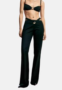 Schwarzes zweiteiliges Outfit mit einem Bandeau-Top mit goldener Schnalle und hochtaillierter Hose mit Ausschnitten und einem ähnlichen goldenen Akzent.