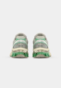 Running shoes in light gray with green accents, featuring a mesh upper, padded collar, and a thick, textured rubber sole.