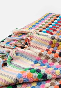 Colorful woven blanket featuring a textured polka dot pattern in various hues. Edged with striped tassels in pastel colors.