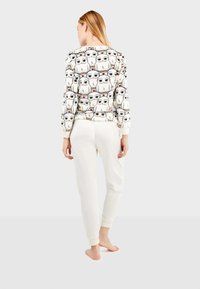 Blusa de manga larga de tela blanca con un patrón repetido de búhos de dibujos animados. Combinada con pantalones de chándal de color beige claro y puños visibles.