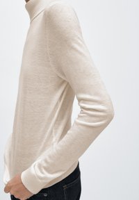 Lichtbeige coltrui gemaakt van een zachte gebreide stof, met smalle lange mouwen en geribbelde manchetten voor een aansluitende pasvorm.