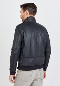 Marine leren bomberjack met geribde zoom en manchetten, featuring een staande kraag en zichtbare stikdetails. De achterkant toont een gladde textuur.