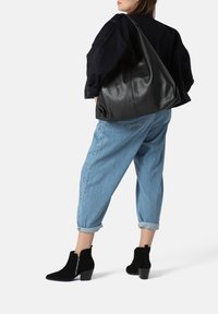 Borsa hobo nera in pelle con finitura testurizzata, abbinata a jeans in denim azzurro a risvolto e stivali neri alla caviglia con dettaglio zip.