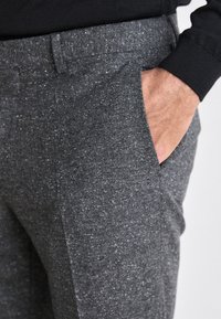 Pantaloni grigi a trama con un motivo maculato, dotati di tasche laterali e una vestibilità sartoriale. Il materiale sembra morbido e intrecciato.