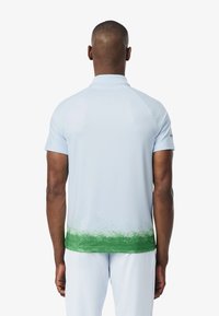 Ljusblå pikétröja med korta ärmar, grön gradient vid sömmen, mjukt tyg och en kragsdesign. Minimal detaljer på baksidan.