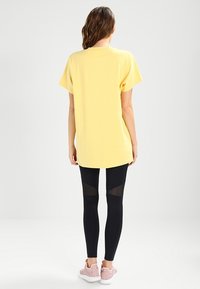 Yellow cotton t-shirt with short sleeves, paired with black leggings featuring mesh panels. Pink shoes complete the outfit.