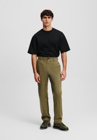 Cammicia nera a maniche corte con motivo testurizzato, pantaloni verde oliva e scarpe verde scuro. Stile semplice e aderente con una silhouette classica.