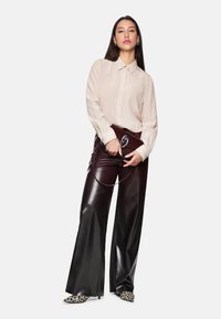 Beige long-sleeve shirt with a button placket, paired with high-waisted burgundy leather pants and pointed leopard-print heels.