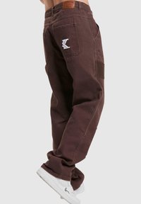 Brune cargo bukser med afslappet pasform og sidelommer. Har et lædermærke og hvidt logo på baglommen. Lavet af bomuldsmateriale med en glat tekstur.