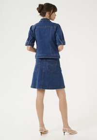 Denim jasje met pofmouwen en een getailleerd ontwerp, gecombineerd met een bijpassende denimrok. Beide in donkerblauw met contrasterende stikseldetails.