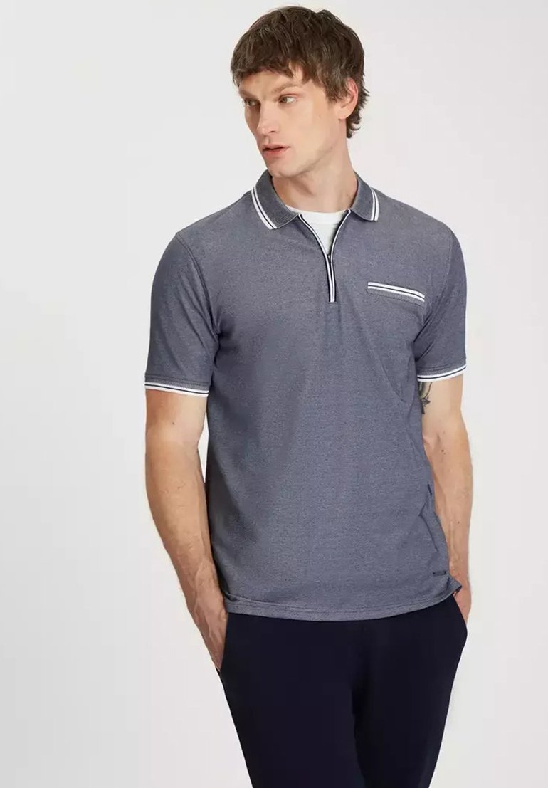 Szara koszulka polo z krótkimi rękawami, zapięciem na dwa guziki oraz białymi wykończeniami kołnierza i rękawów. Posiada kieszonkę na piersi z białym paskiem.